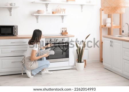 Young woman opening electric oven in kitchen Royalty-Free Stock Photo #2262014993