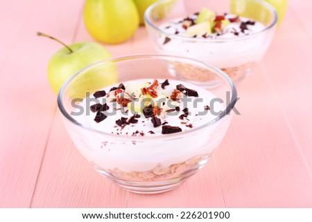 Oatmeal with yogurt in bowls, apples and walnuts on pink wooden background