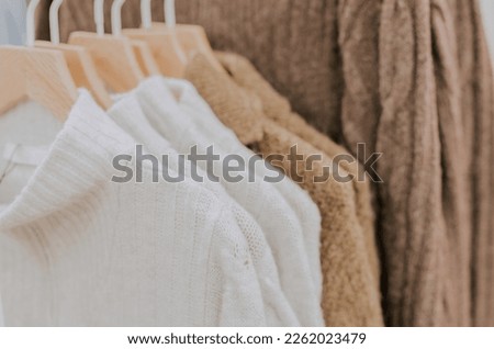 White knitted turtleneck sweaters and brown cardigans hang on hangers on a stand in a clothing store, close-up side view with selective focus.Offline shopping concept.