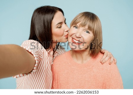 Close up elder parent mom with young adult daughter two women together wear casual clothes doing selfie shot pov on mobile cell phone kiss hug isolated on plain blue cyan background Family day concept