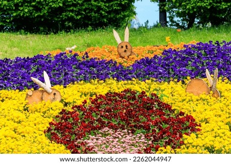 Colorful flowerbed of pansies and daisies decorated with wooden Easter bunnies in park at spring