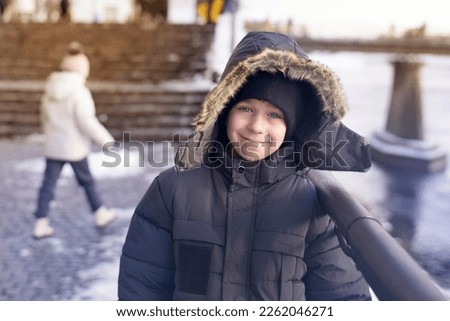 Portrait of a cute happy boy in winter in the city near the river, the boy is warmly dressed and not cold, he was born in the winter and loves winter and winter games in outside very much