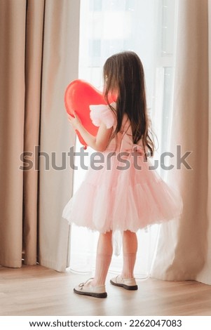 valentine's day baby. A little girl in a red dress holds a large ball in the shape of a heart