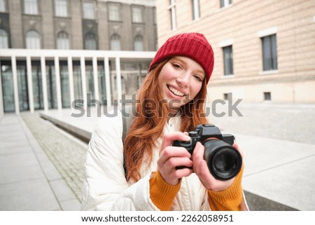 Beautiful readhead girl, photographer with professional camera takes pictures outdoors, walking around city and taking photos, sightseeing.