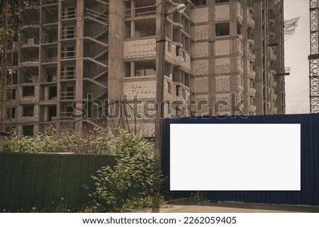 Large white banner with empty place for mockup fixed on fence of construction site. Blank poster for information under unfinished house outdoor.