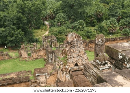 A photo taken from the top of the main pyramid at the Pre Rup Temple site. The view here looks out over the rear entrance and a path leading to the jungle. A statue and collapsed tower are visible. 