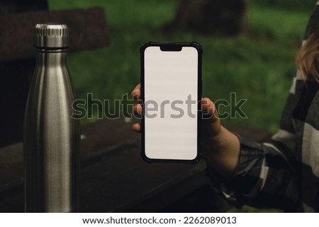 Mobile phone social media White screen Template for mobile app. Reusable steel thermo water bottle on wooden bench. Sustainable lifestyle. Plastic free zero waste free living. Go green Woman student 