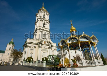 White orthodox church with gold domes near the source of holy water on the background of blue sky.
