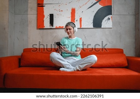 One woman sit on the floor at home with headphones use smart-phone for music listening or search for podcast online meditation or audiobook on her smarphone mobile phone online on internet copy space