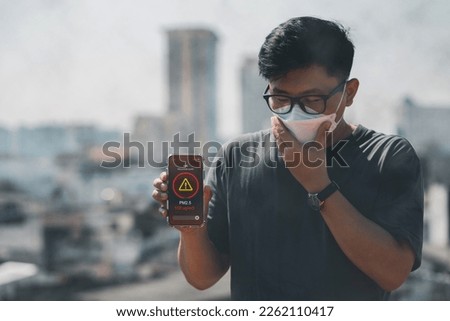 Man wearing the N95 Respiratory Protection Mask and using a smartphone app showing PM 2.5 dust in the capital that exceeds the standard that is harmful to health. air pollution concept, pm 2.5 warning Royalty-Free Stock Photo #2262110417