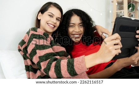 Happy young girlfriends couple hugging having fun using digital tablet relaxing on bed at home. Two smiling women friends holding computer looking at screen enjoying surfing online watching videos.