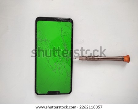 black smartphone with green screen and cracked screen due to being pricked by screwdriver - isolated on white background