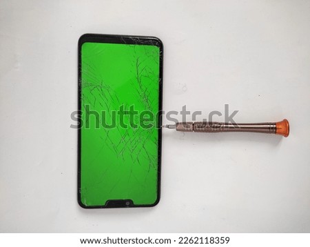 black smartphone with green screen and cracked screen due to being pricked by screwdriver - isolated on white background