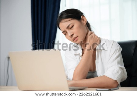Office syndrome concept. Young asian woman feeling pain in neck and shoulder after working on computer laptop for a long time. She stretches to relax her muscles Royalty-Free Stock Photo #2262121681
