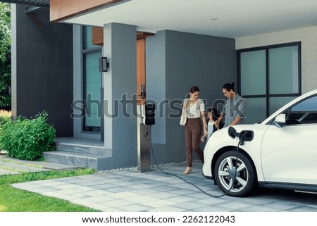 Progressive young parents and daughter with electric vehicle and home charging station. Green and clean energy from electric vehicles for healthy environment. Eco power from renewable source at home. Royalty-Free Stock Photo #2262122043