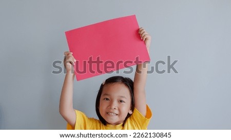 Portrait of a young asian little girl holding red paper blank sign over gray background