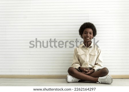 Portrait of black african american cute little boy child sitting on floor on white wall background