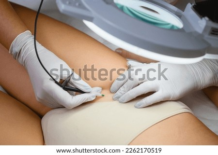Electrolysis professional hair removal in bikini zone, cosmetologist hands in gloves work on female skin close up