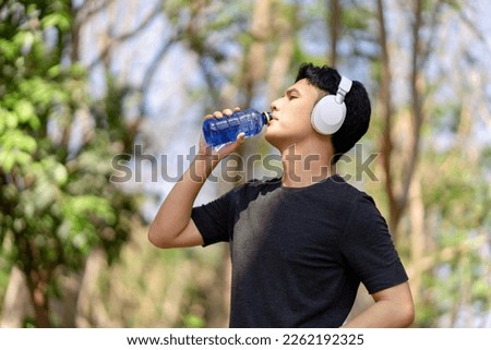 Male runner drinking water after running at green park Royalty-Free Stock Photo #2262192325