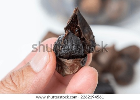 Closed up picture of someone hand holding peel black garlic with blur background of black garlic heaps.