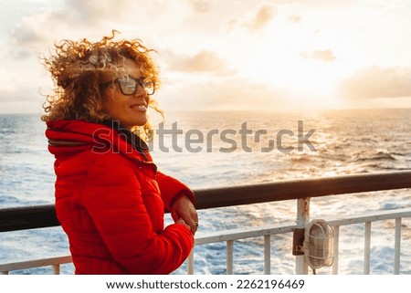 Cruise ship vacation woman enjoying sunset on travel at sea. Traveler happy woman in red jacket looking at ocean relaxing on luxury cruise liner boat. People and ferry boat transport. Travel activity Royalty-Free Stock Photo #2262196469