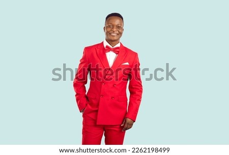 Portrait of attractive, elegant and stylish dark-skinned male showman or host of festive event on pastel gray background. Smiling man in red classic suit and with bow tie looks confidently at camera.