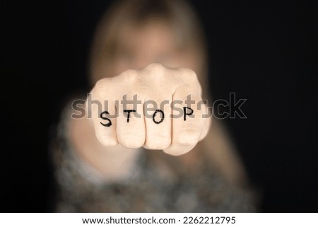 Woman with closed fist with word STOP written to campaign against gender violence and pain. Hand raised and punch to dissuade for self harm awareness, stop abusing, bullying, mental health. Copy space Royalty-Free Stock Photo #2262212795