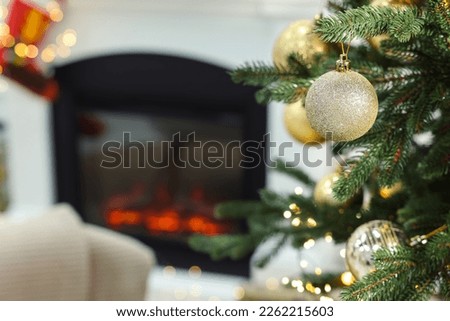 Beautiful Christmas baubles hanging on fir tree branch in room, space for text