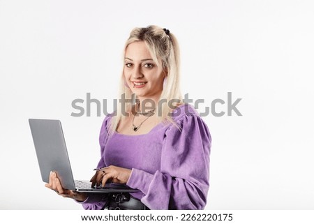 Cheerful blonde woman blouse isolated over white background holding a laptop, smiling at the camera with a confident expression. Typing on laptop keyboard. Creating web design or digital work.