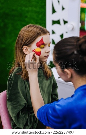 A professional make-up artist, artist paints with a brush on her face with face paints, drawing, children's makeup for a little girl model, a child. Photography, art, concept, lifestyle. Royalty-Free Stock Photo #2262237497