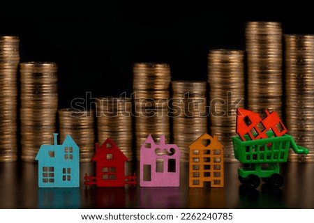 Multi-colored miniature symbolic houses against the background of columns of gold coins