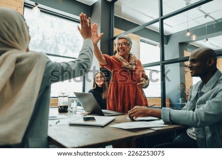 Two successful businesswomen high fiving each other during an office meeting. Cheerful businesswomen celebrating their achievement. Happy businesspeople working as a team in a multicultural workplace. Royalty-Free Stock Photo #2262253075