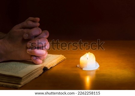 Religious concepts.The young payer prayed on the Bible in the room and lit the old candle to illuminate.Dark religion room.