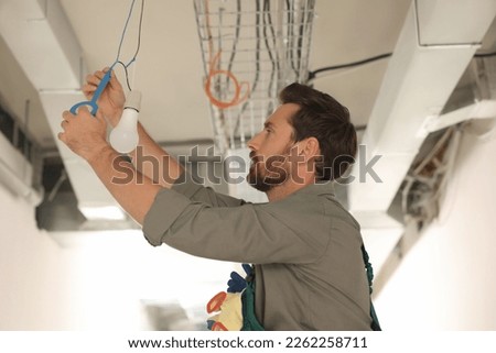 Electrician with insulting tape repairing ceiling lamp Royalty-Free Stock Photo #2262258711