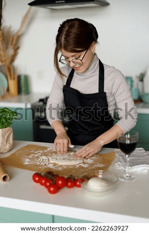 A woman in an apron cooks margarita pizza in the home kitchen. Kneads the dough.