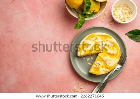 Lemon cheesecake tart or pie, with fresh lemons and cup of coffee, pink background. Copy space