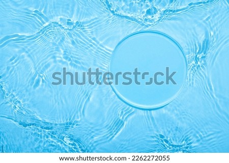 Empty clear glass circle podium on blue transparent calm water texture with waves in sunlight. Abstract nature background for product presentation. Flat lay cosmetic mockup, copy space. Royalty-Free Stock Photo #2262272055