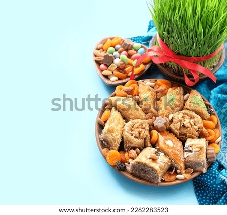 Nowruz festive table. green wheat grass with red ribbon, dessert baklava, sweets, nuts, dry fruits on abstract blue background. Spring equinox in March, Nowruz Holiday. copy space
