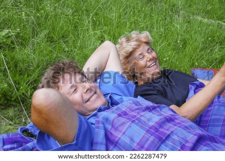 Happy elderly couple lying on the lawn with the blanket, active seniors relaxing.