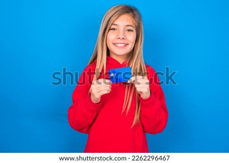 Photo of caucasian teen girl wearing red sweater over blue wall positive smile hold credit card income salary