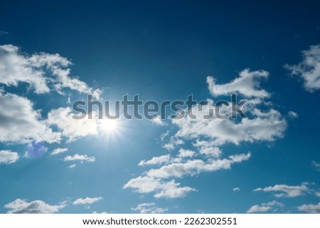 The blue summer sky with white fluffy clouds. Sunbeam through the haze on blue sky