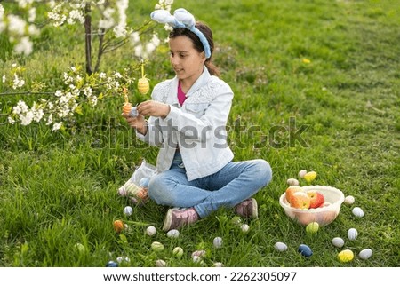 little girl wearing bunny ears with colorful Easter eggs outdoors on spring day