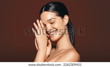 Woman with flawless skin radiating happiness and self-confidence. Young gen z woman smiles as she shows off her beautiful skin in a studio. This woman enjoys maintaining a consistent skincare routine.