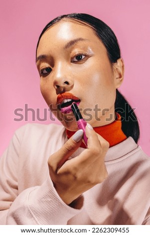 Portrait of a young woman applying a two-toned lipstick, she looks at the camera with confidence. Woman creating a trendy, bold look on her face with self-assurance. Royalty-Free Stock Photo #2262309455