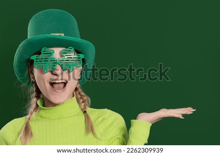 St. Patrick's Day leprechaun model girl in green hat, funny clover shaped sunglasses, isolated on green background and smiling, having fun. Patrick Day pub party, celebrating. 