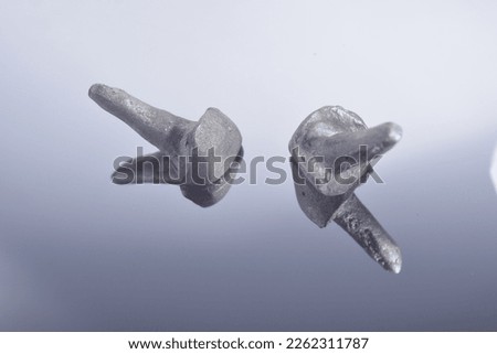 Two cast metallic post and core for crown reconstruction build-ups or inlay cores for incisor tooth manufactured with nickel chrome alloy. Mirror reflection macro-photography natural grey scaled color Royalty-Free Stock Photo #2262311787