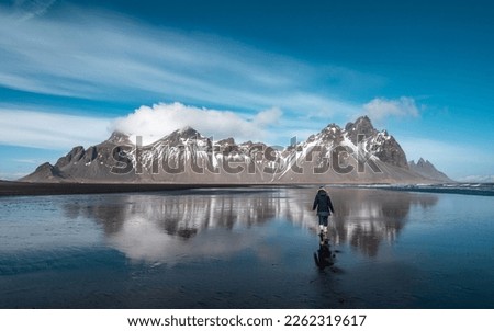 Young girl standing on the reflection of the sea water with the snow capped mountains of Stockness in the background. Iceland Royalty-Free Stock Photo #2262319617