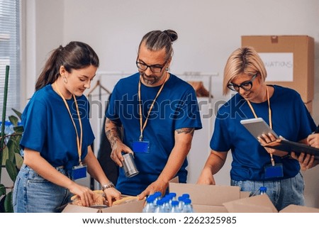 Team of volunteers working at charity organization and wearing blue t shirt while packing clothes and food grocery in donations box. Volunteering, social help for poor and needy. Copy space. Royalty-Free Stock Photo #2262325985