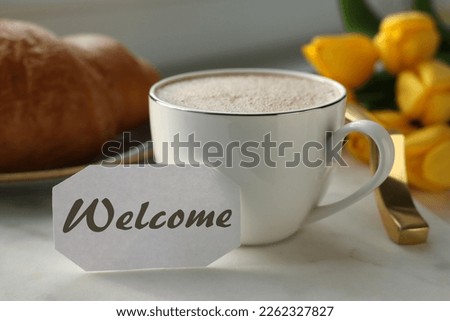 Welcome card, cup of aromatic coffee and croissant on tray and beautiful yellow tulips