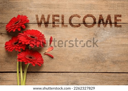 Welcome card. Beautiful red gerbera flowers and word on wooden table, top view